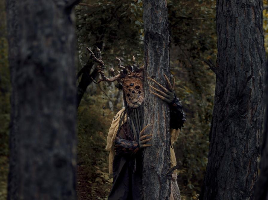 Uhyggelig maskeklædt træmand foran gammelt træ